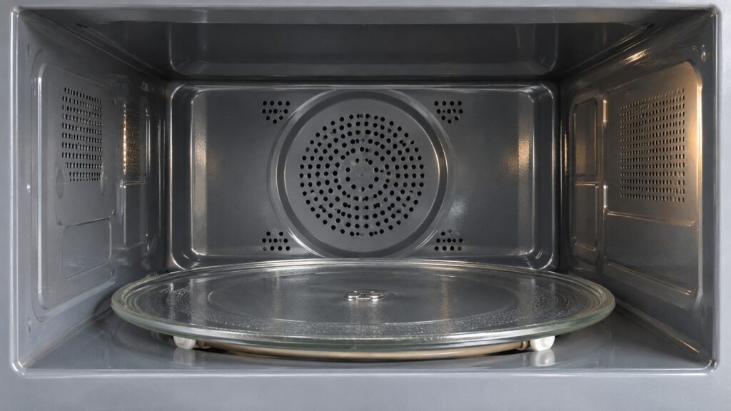 The interior of an empty microwave cavity showing the rear convection fan cover and the glass turntable